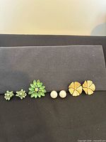 Row showing green rhinestone earrings, brooch, white ball studs, cream flower earrings