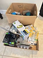 Two boxes containing Makita sander, Philips bulb box, Noma bulb boxes, casters and other hardware