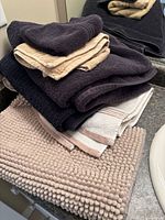 Stack of black, white-beige and beige towels with beige chenille bath mat on countertop