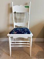 Full front view of white wooden chair showing carved back, spindle design, floral seat pad