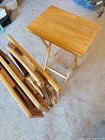 Set of four folded TV trays and one opened next to storage rack