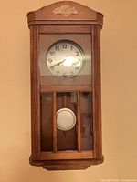 Frontal view showing entire wall clock, dial, glass door, pendulum