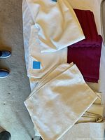 Stack showing white, burgundy, ivory jacquard tablecloths and beige table pads