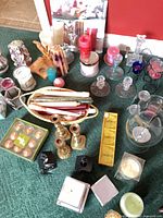 Overview of lot with brass candlesticks, basket of tapers, clear glass candlesticks, boxed tealights, hurricane shade, various candles