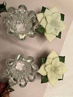 Two clear glass candle holders beside two white wax poinsettias