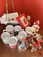 Group shot of mugs, basket, linens, pillow, snowman, ornaments