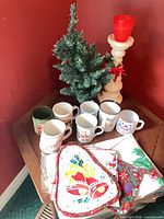 Group shot showing tree, candle holder with red glass, mugs, linens