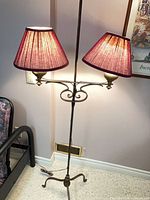 Full view of two-shade floor lamp illuminated beside bed