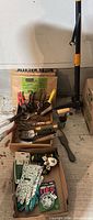 Overall view of tools arranged in trays including loppers, pruners, trowels, bulb planter, gloves, hose accessories and yard bags