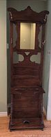 Full view of tall wooden hall tree with mirror, hooks, shelf, and base
