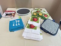 Lot overview with towels, pot holders, oven mitt, lazy susan, burner liners package, cutting board