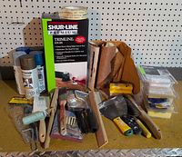 Assortment of painting tools, spray paint cans, Shur-Line box, sandpaper, brushes and accessories on work surface
