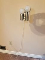Full view of one chrome mid-century wall sconce plugged in and illuminated