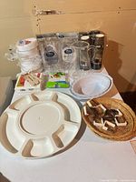 Overall lot showing packed plates, glasses, cups, bowls, pitcher, snack tray, wicker platters and tablecloth clips