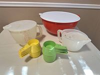 Overall lot showing Thatsa Bowl, Mix-N-Stor pitcher, small pitcher with lid, two sets of measuring cups