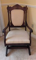 Front view of carved wood rocking chair with cream upholstery