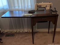 Sewing machine mounted in wooden cabinet table with leaf extended