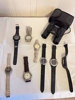 Overview of binoculars and eight watches laid out on table