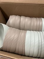 Stacks of ribbed light taupe and light aqua plastic bowls inside cardboard box