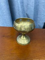 Side view showing brass diya with swastika motifs and pedestal base