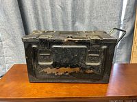 Front view of closed metal ammunition box showing paint wear and clasp