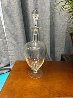 Full view of clear glass decanter with stopper on wooden surface