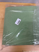 Folded green ribbed mat in plastic wrap, barcode label visible