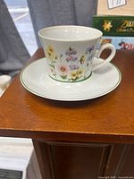Teacup on saucer showing floral design and green rim