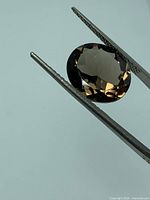 Loose oval smoky topaz held in gem tweezers