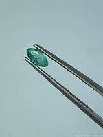 Marquise emerald gripped by tweezers, side view