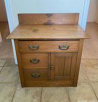 Front view of oak wash stand cabinet with drawers, door, and backsplash