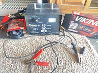 Overall lot showing Sears charger, Viking boxed charger-maintainer, packaged booster cables, and charger leads