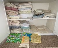 Full view of cabinet shelves showing folded stacks of sheets, pillowcases, and mattress protector