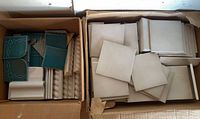 Two boxes showing beige square tiles and assorted teal and trim pieces