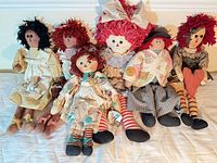 Group of six Raggedy Ann and Andy style dolls seated on bed