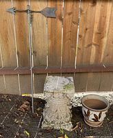 Weather vane, stone pedestal and ceramic pot arranged together for scale