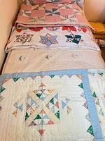 Stack of quilts and pillowcases on bed showing patterns and colours