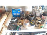 Shelf with masking paper rolls, foam tape package, assorted tape rolls, wire spools, multiple spray cans