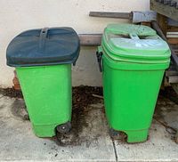 Two green wheeled trash cans side by side on driveway