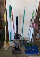 Group shot of Shark vacuum, string mops, broom with dustpan, flat mop, large dustpan scoop, microfiber pads