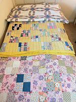 Three quilts layered on bed: double wedding ring, yellow patchwork, pink-lilac patchwork
