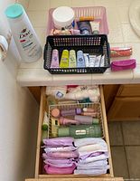 Full lot showing Dove body wash, CeraVe cream, travel-size toiletries, baskets, open drawer with Clinique bottles, cotton balls and sanitary pads