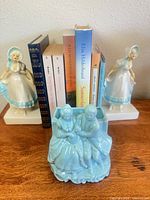 Books flanked by ceramic lady bookends; blue courting couple planter in foreground