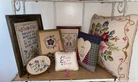 Overview of all framed cross-stitch pieces and pillows on shelf