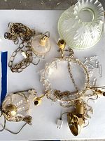 Assorted chandelier parts laid out on table: two mini fixtures, brass ring frame, glass shade, loose prisms and chains