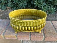 Top and side view of olive-green Maurice of California ceramic planter on brick ledge