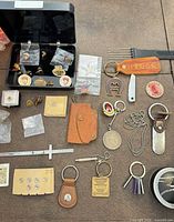 Overall lot view showing pins in plastic case, keychains, caliper, cufflinks, shirt studs