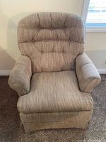Front view of beige upholstered swivel rocker with tufted back and padded arms