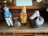 Group shot of sailor figurine, glass whale, fisherman figurine, carved wood duck on shelf
