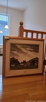 Full view of framed painting leaning against railing showing entire artwork and frame
